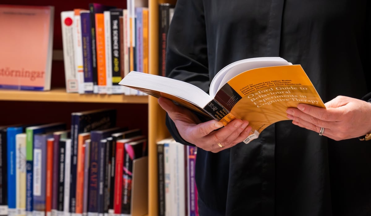 En person som står framför en bokhylla med en bok i handen.